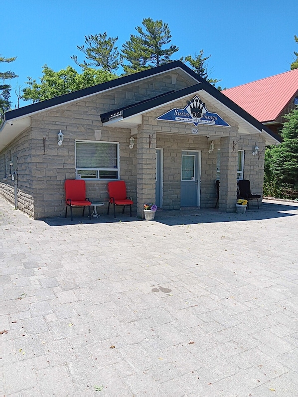 A stone building with a red roof, a sign for 'Suites of Wasaga', and two red chairs outside.