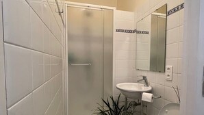 Une petite salle de bain avec des carreaux blancs, une douche en verre, un lavabo blanc et des toilettes.