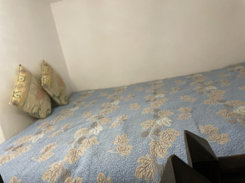En säng med ett blått, blommigt överkast och två kuddar med liknande mönster.