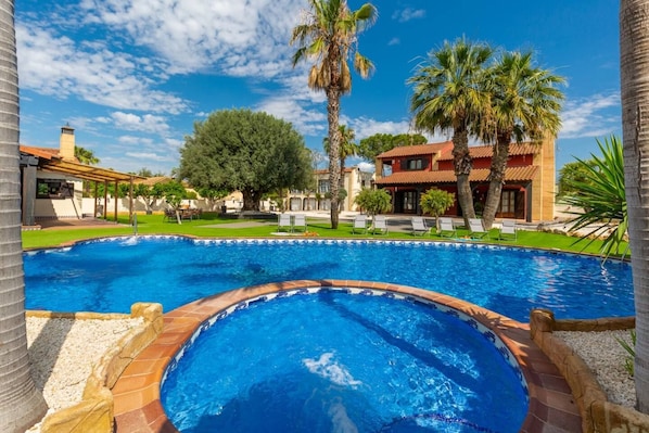 A swimming pool with a tiled edge, surrounded by palm trees and a building with a red roof.