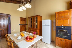 A kitchen with wooden cabinets, a white refrigerator, and an oven. There is a dining table with a fruit bowl and cups. - Summer Dream by Fidalsa (Catral)
