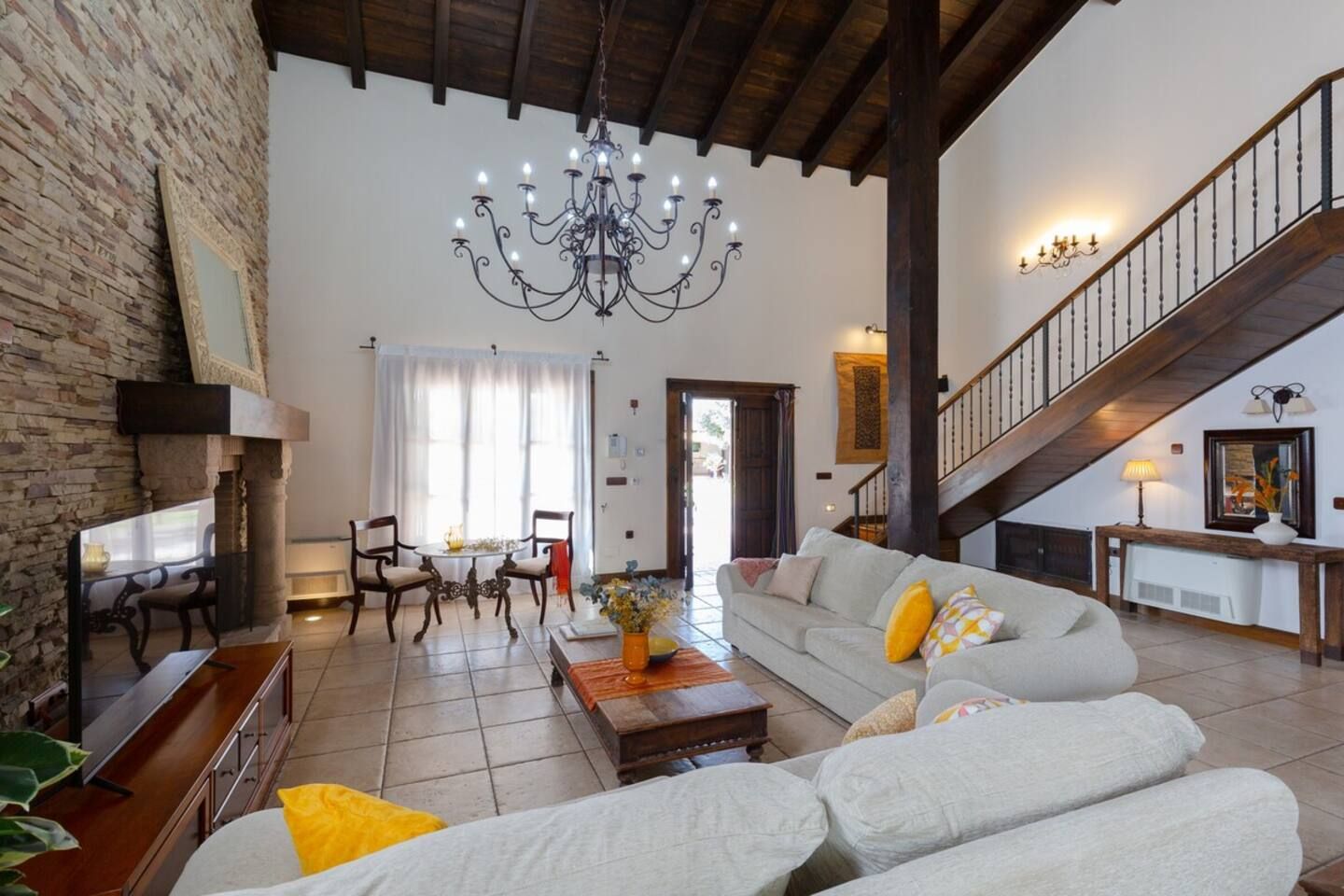 Un vaste salon doté d’un haut plafond, d’un lustre, d’un escalier et d’un coin repas avec des chaises et une table.