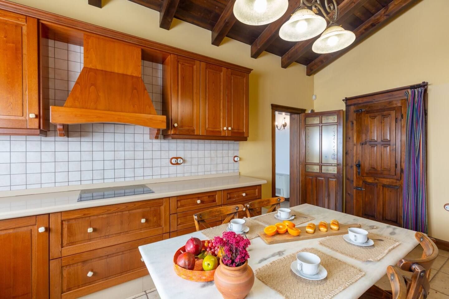 Une cuisine avec des meubles en bois, un plan de travail en marbre et une table à manger mise avec des tasses et un saladier de fruits.