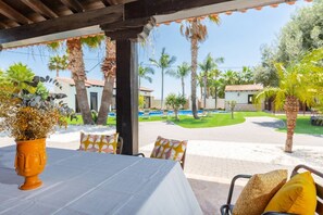 A covered outdoor seating area with a table, chairs, and a decorative plant.