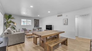 A spacious living room with a wooden dining table, a sofa, and a TV. - Remodeled Gem w/ bocceball - 8 Minutes to Oldtown (Scottsdale)