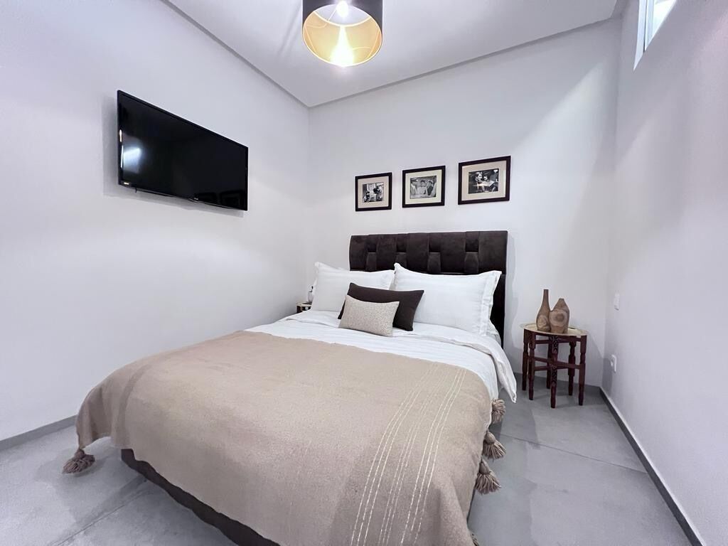 Ein modernes Schlafzimmer mit einem Bett, einem flachbildfernseher an der Wand und drei gerahmten Bildern über dem Bett.