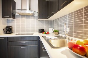 Une cuisine moderne avec des meubles de couleur sombre, un évier en acier inoxydable et un dosseret carrelé.