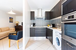 Une cuisine moderne avec des meubles de couleur sombre, un lave-linge encastré et un coin repas comprenant un canapé et une table.