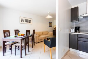 A dining area with a table, chairs, and a sofa. There is a kitchen area with cabinets and a countertop.