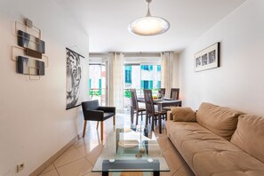 Un salon moderne avec une table basse en verre, un canapé beige et un coin repas comprenant des chaises et une table.