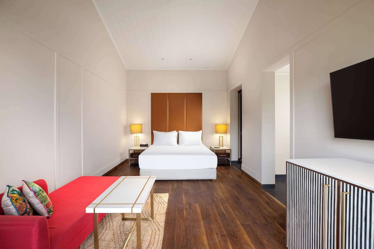 Ein Hotelzimmer mit einem großen Bett, Nachttischen mit Lampen, einem roten Sofa, einem kleinen Tisch und einem Fernseher an der Wand.
