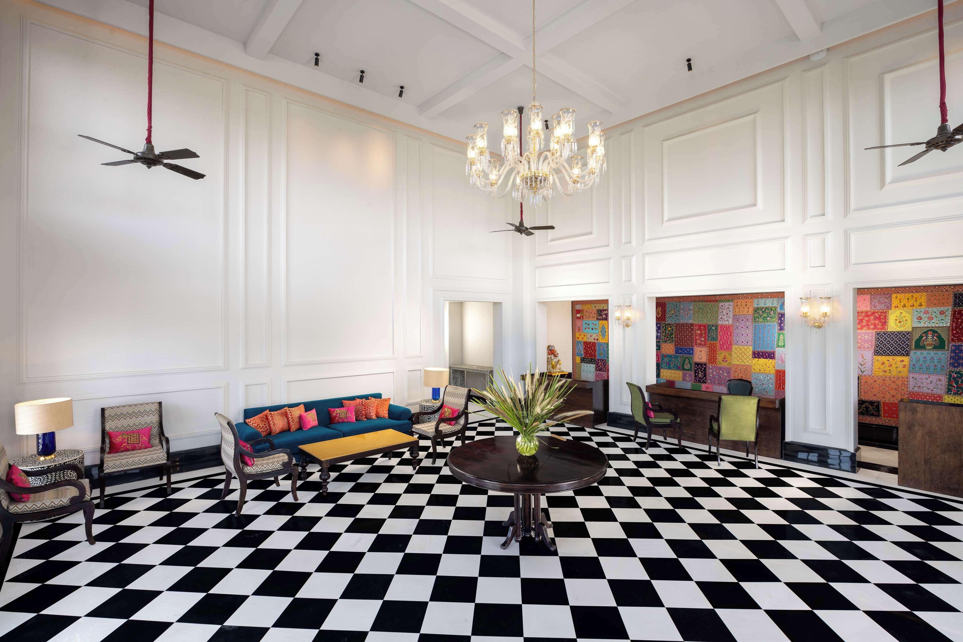 A lobby with a black and white checkered floor, a chandelier, a blue sofa with colorful cushions, and a reception desk.