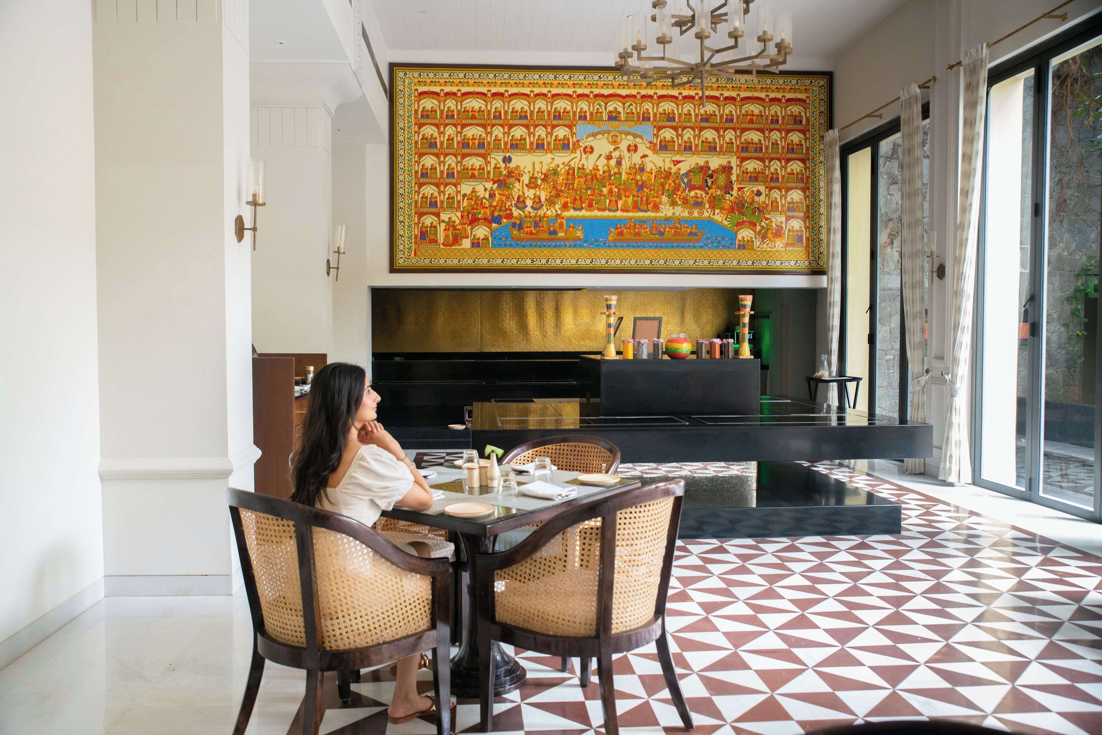 A dining area with a large, ornate tapestry on the wall, a modern chandelier, and a patterned floor.