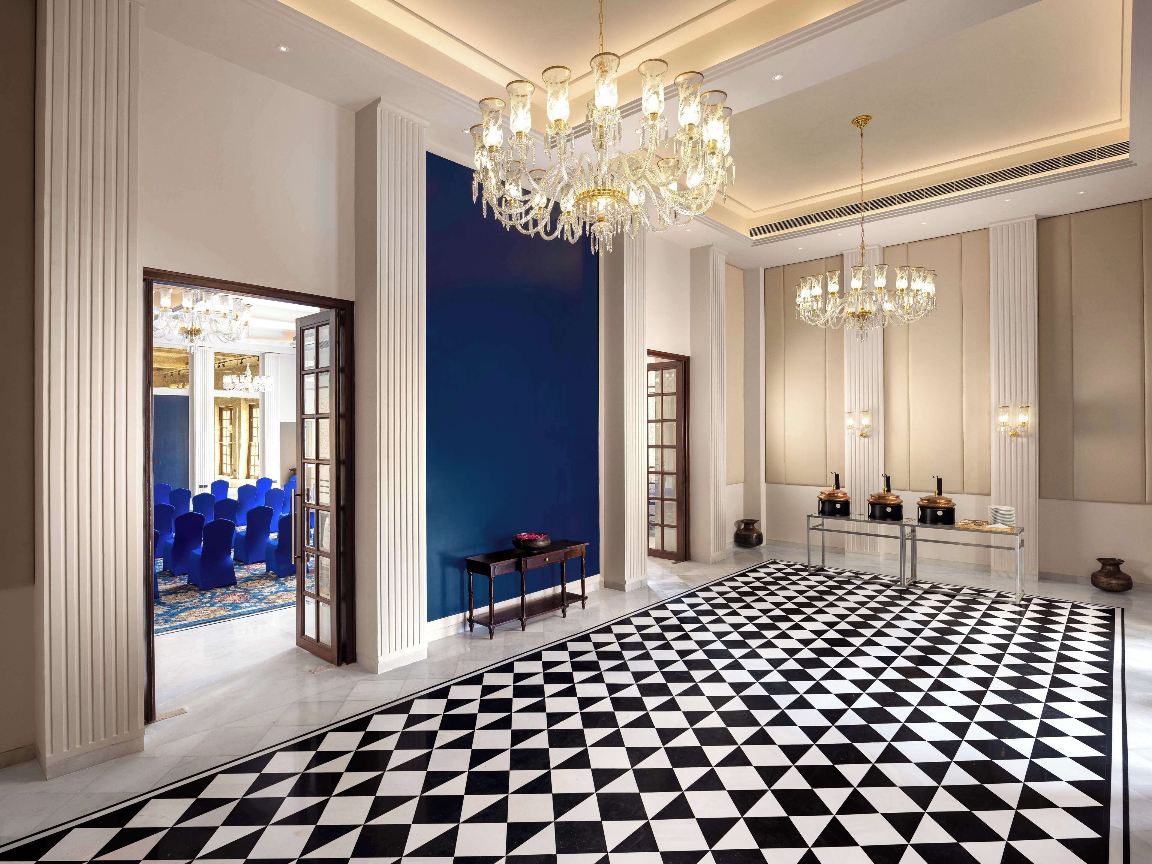 A spacious lobby with a black and white checkered floor, a grand chandelier, and a seating area with blue chairs.