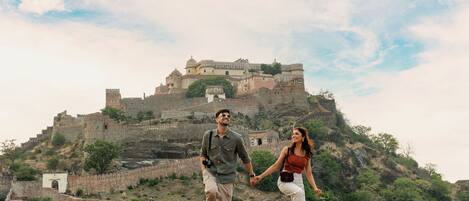 Una pareja camina por un sendero de piedra con una fortaleza histórica al fondo.