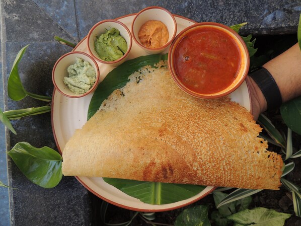 Un plato con una dosa, chutney de coco, sambar y un pequeño cuenco de raita.