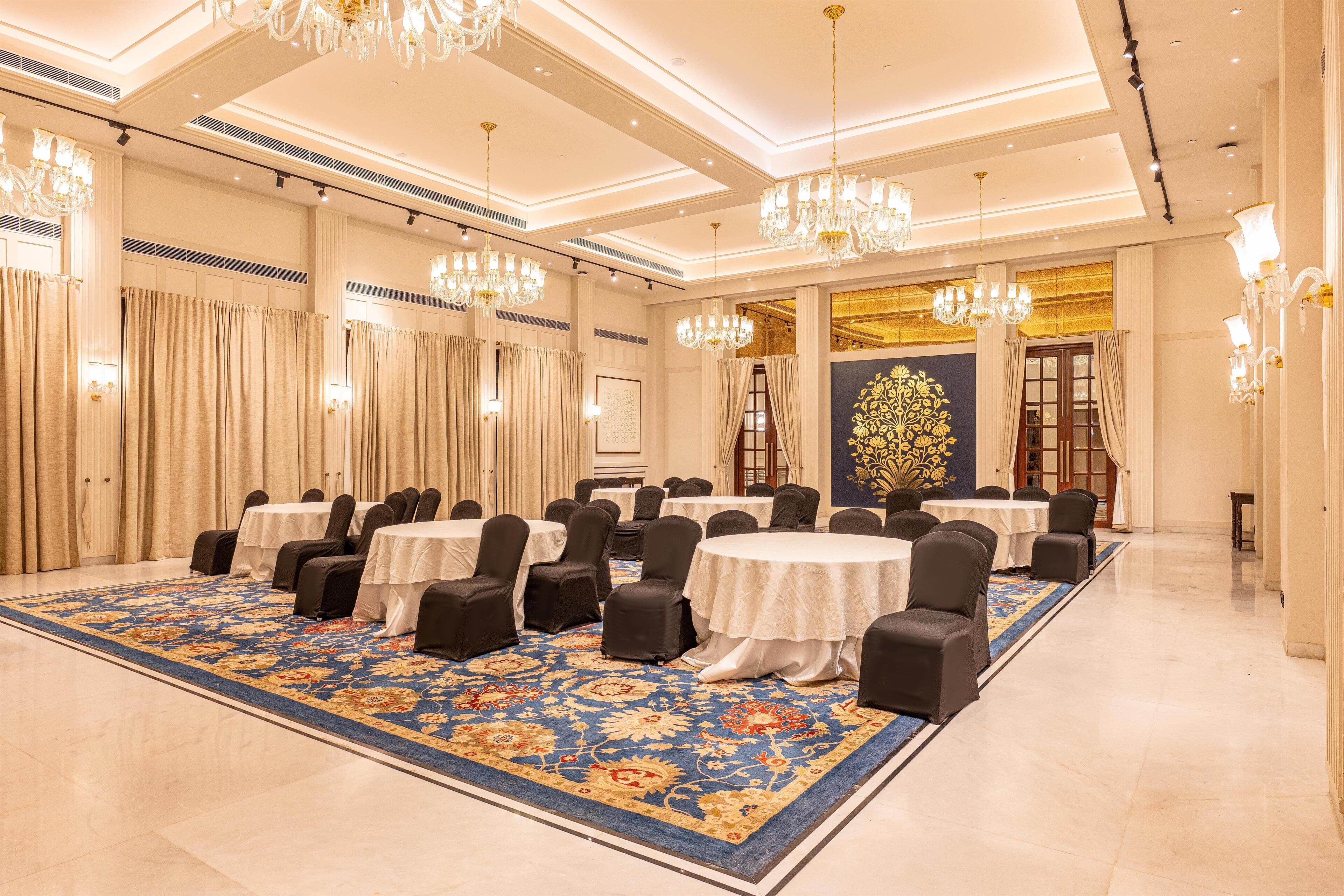 Un salón de conferencias con mesas redondas, sillas negras, candelabros y una alfombra estampada.