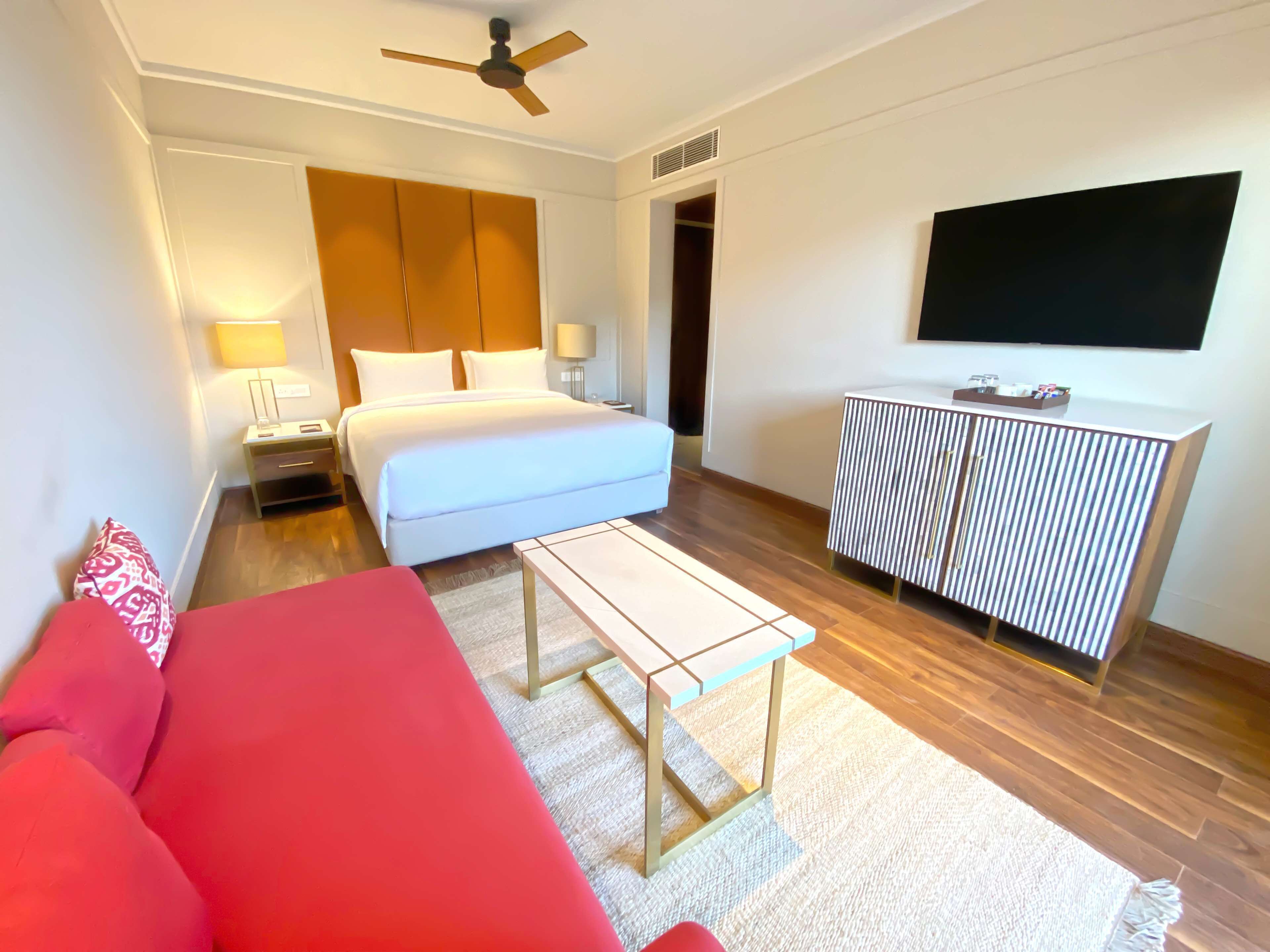 A hotel room with a bed, a red sofa, a small table, a TV, and a radiator.