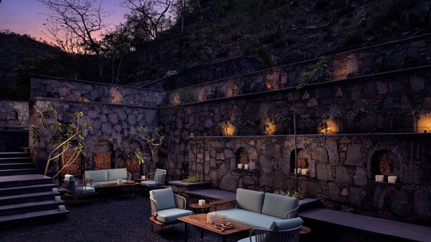 Un patio al aire libre con muros de piedra, mobiliario y luz ambiental.