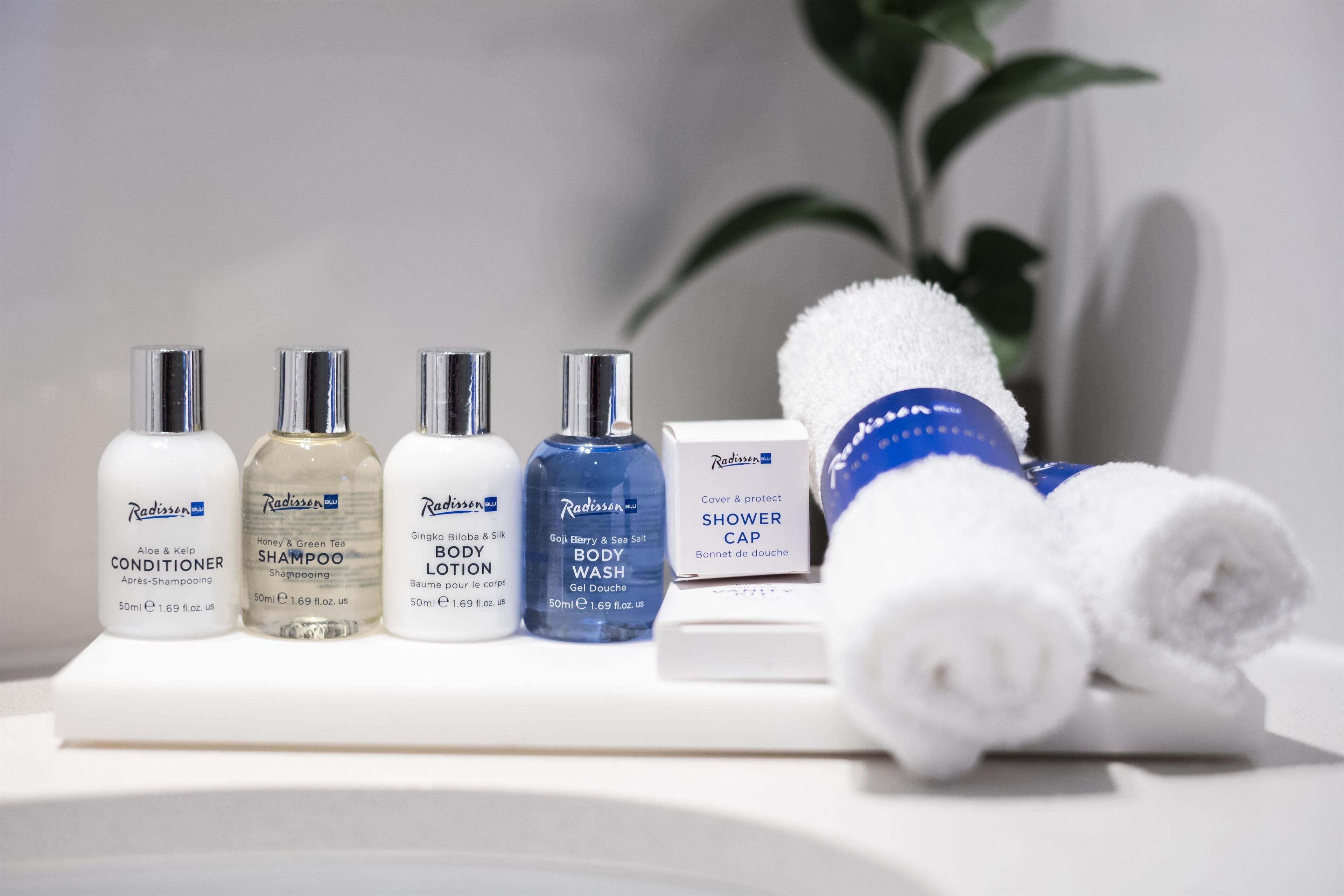 Una encimera de baño con diversos artículos de aseo Radisson, incluyendo acondicionador, champú, loción corporal, gel de ducha y gorro de ducha.