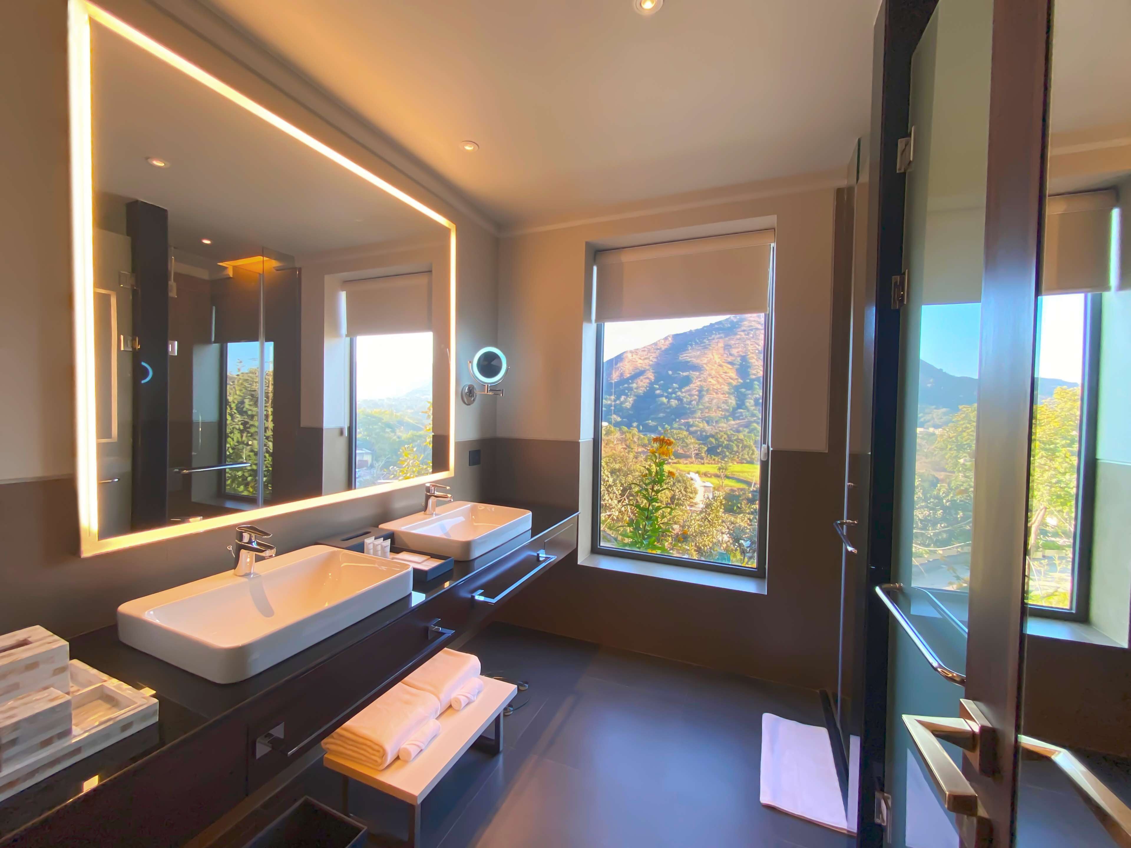 A modern bathroom with two sinks, a large mirror, and a view of a mountainous landscape.