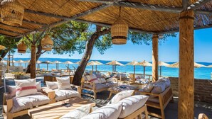 Un salon de plage doté de mobilier en bois et de parasols en chaume, offrant une vue sur la mer.