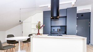 Een moderne keuken met een centraal eiland, een zithoek met een ronde tafel en stoelen, en een decoratieve vaas met gedroogde bloemen.