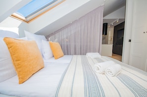 A bedroom with a skylight, a bed with white and blue bedding, and a bathroom visible through an open door.