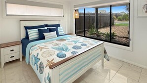 Een slaapkamer met een bed, nachtkastjes, een raam met uitzicht op het buitenleven en een plafondventilator.