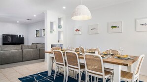 Een moderne eetruimte met een houten tafel en witte stoelen, een geweven hanglamp en kunstwerken met vismotieven aan de muur.