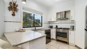 Een moderne keuken met witte kasten, een granieten aanrecht, een gasfornuis, een oven, en een raam met uitzicht op bomen.