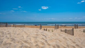 Une plage de sable bordée de clôtures en bois, sous un ciel bleu et dégagé.