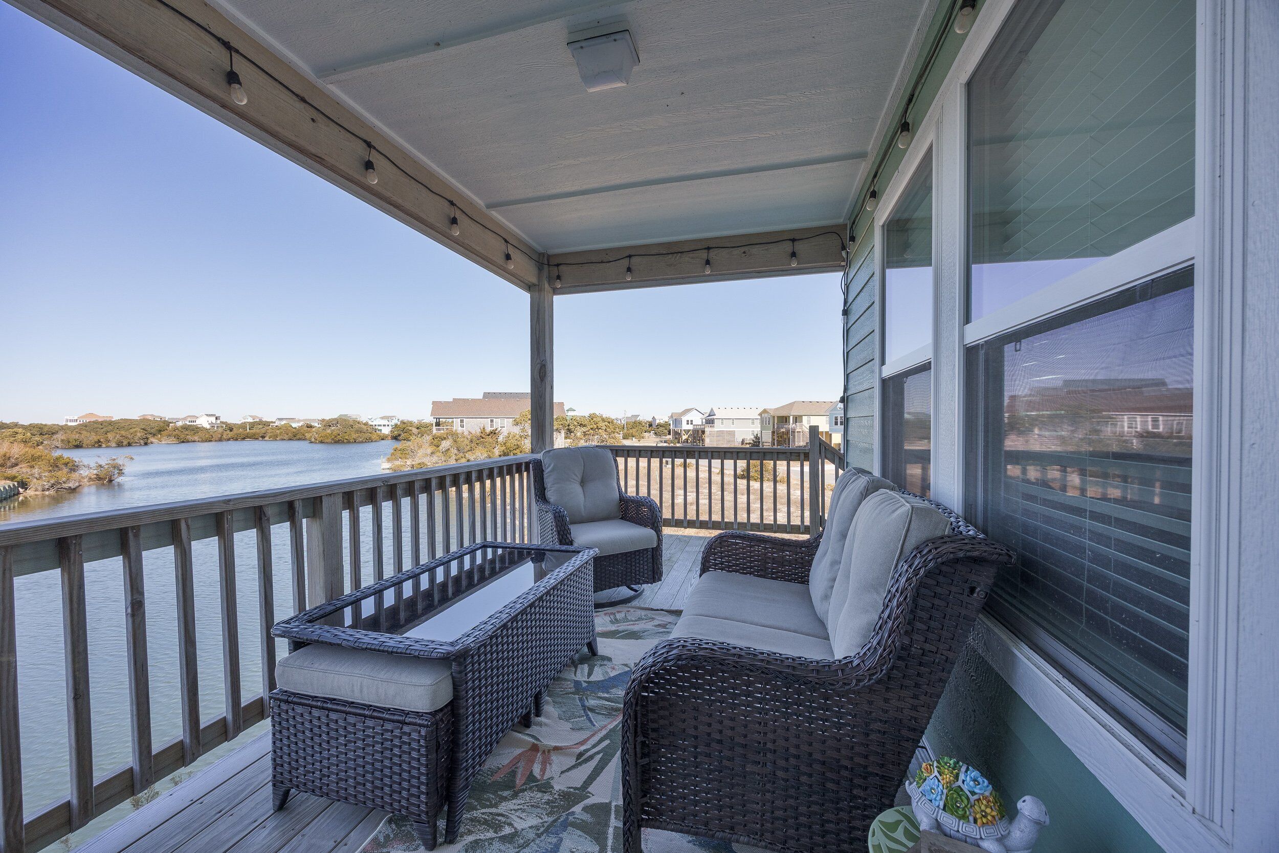 A covered porch with wicker furniture, a view of a body of water, and a railing.
