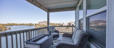 A covered porch with wicker furniture, a view of a body of water, and a railing.