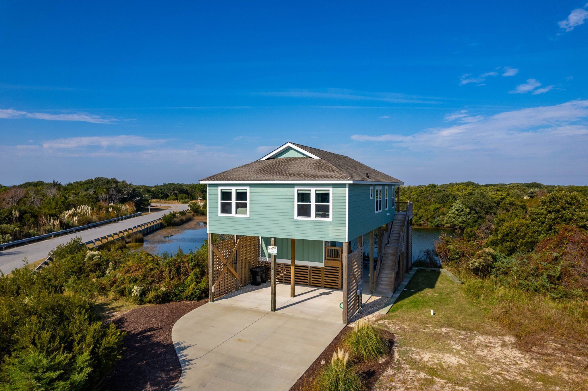 A light blue house with a gabled roof, situated on stilts over a body of water, surrounded by dense greenery.