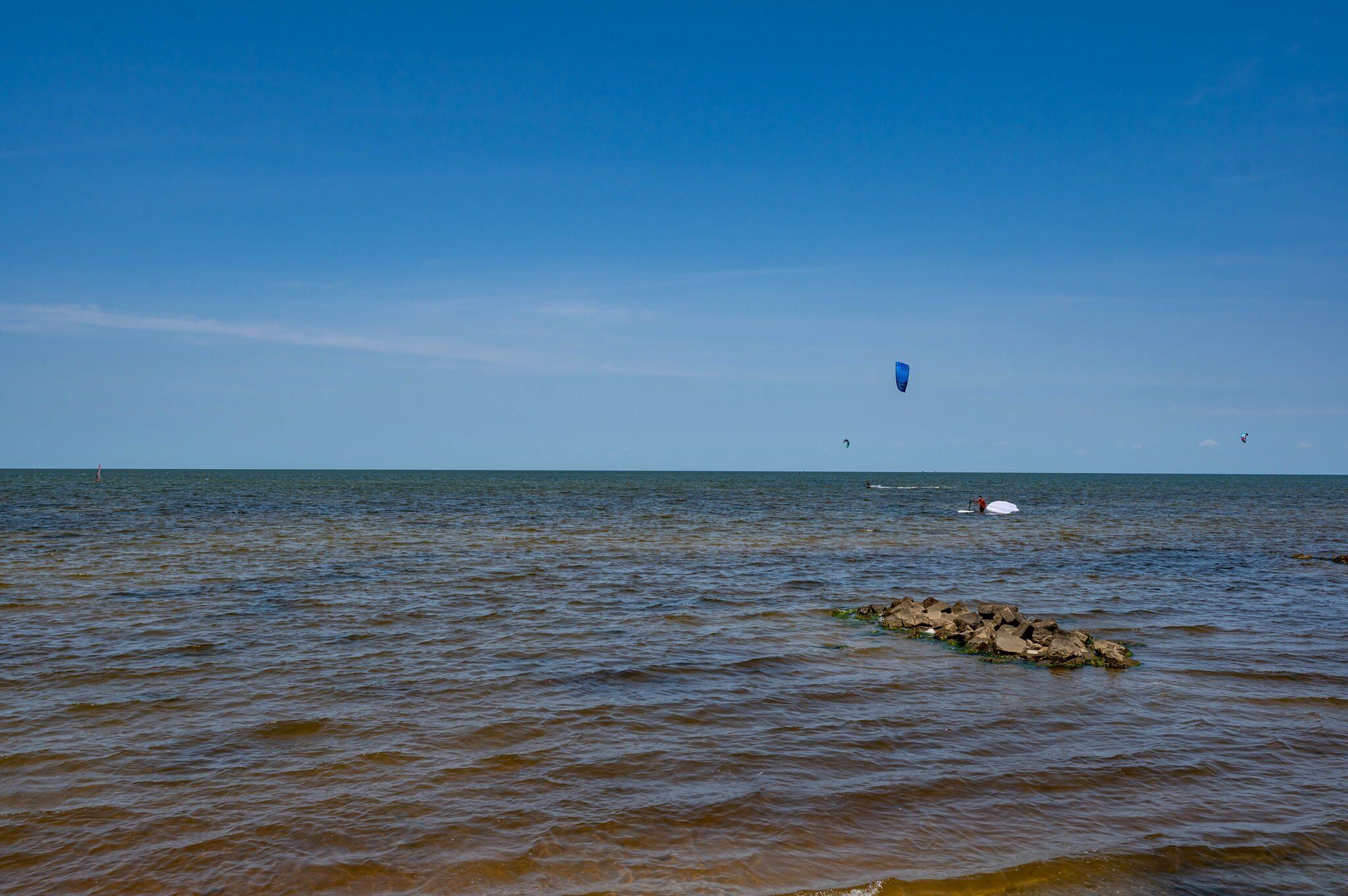 Une mer calme, avec un affleurement rocheux au premier plan et un ciel bleu dégagé.