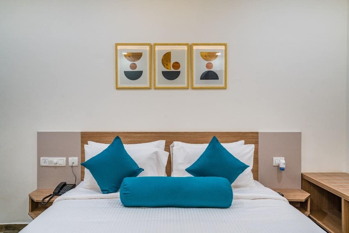 A neatly made bed with white and blue bedding, a wooden headboard, and a bedside table with a phone. Three framed artworks are hung on the wall above the bed.