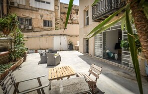 An outdoor patio area with seating, potted plants, and a view of a building with balconies. - Unique and Spacious 2BR Apt with Terrace (Tel Aviv)