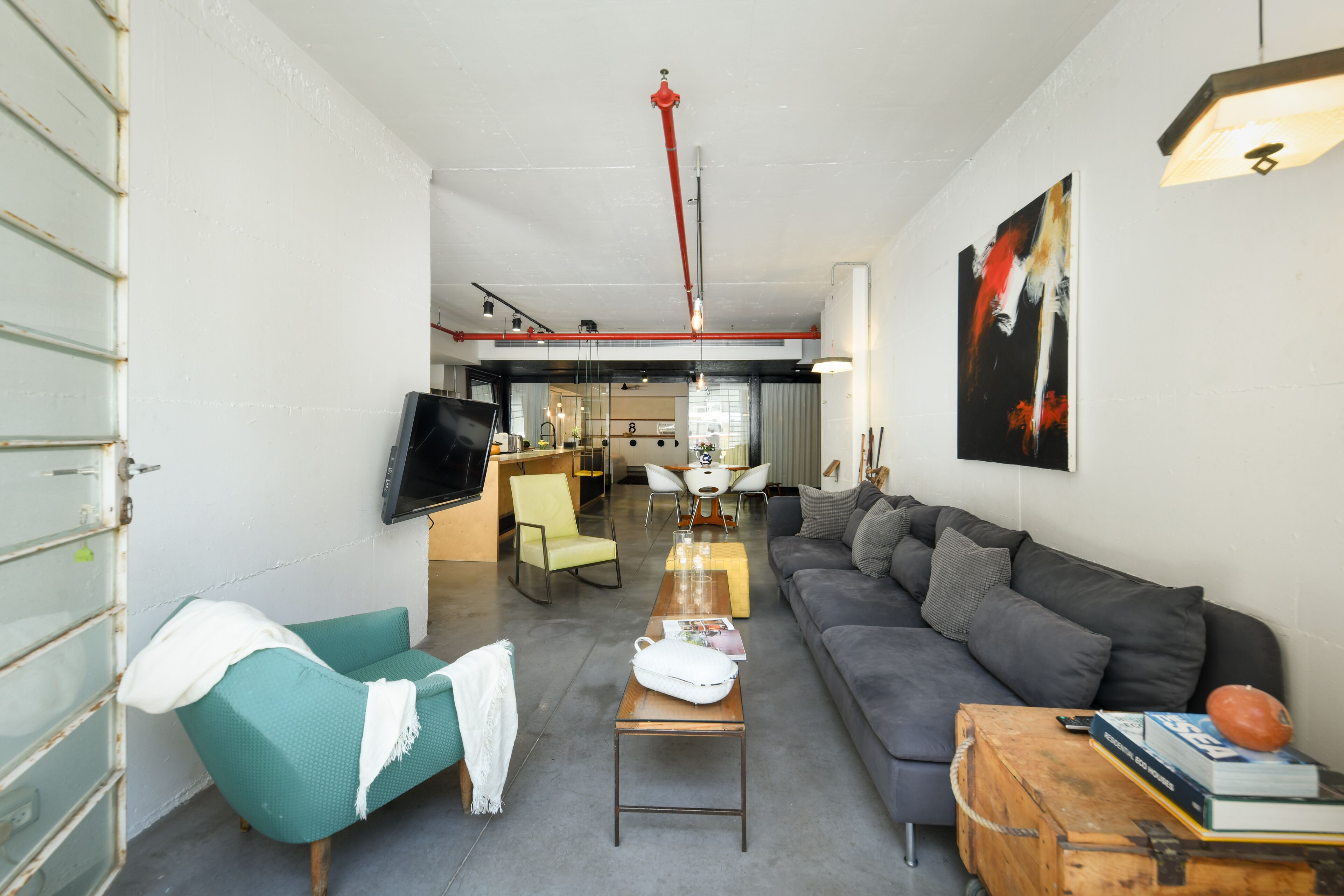 A modern living room with a sofa, a coffee table, and a television. There is a dining area in the background with a table and chairs.