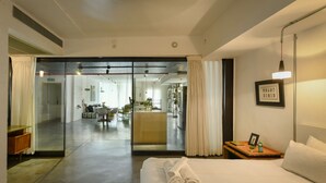 Una habitación de hotel moderna con una cama grande, una mesita de noche con lámpara y vistas al comedor.