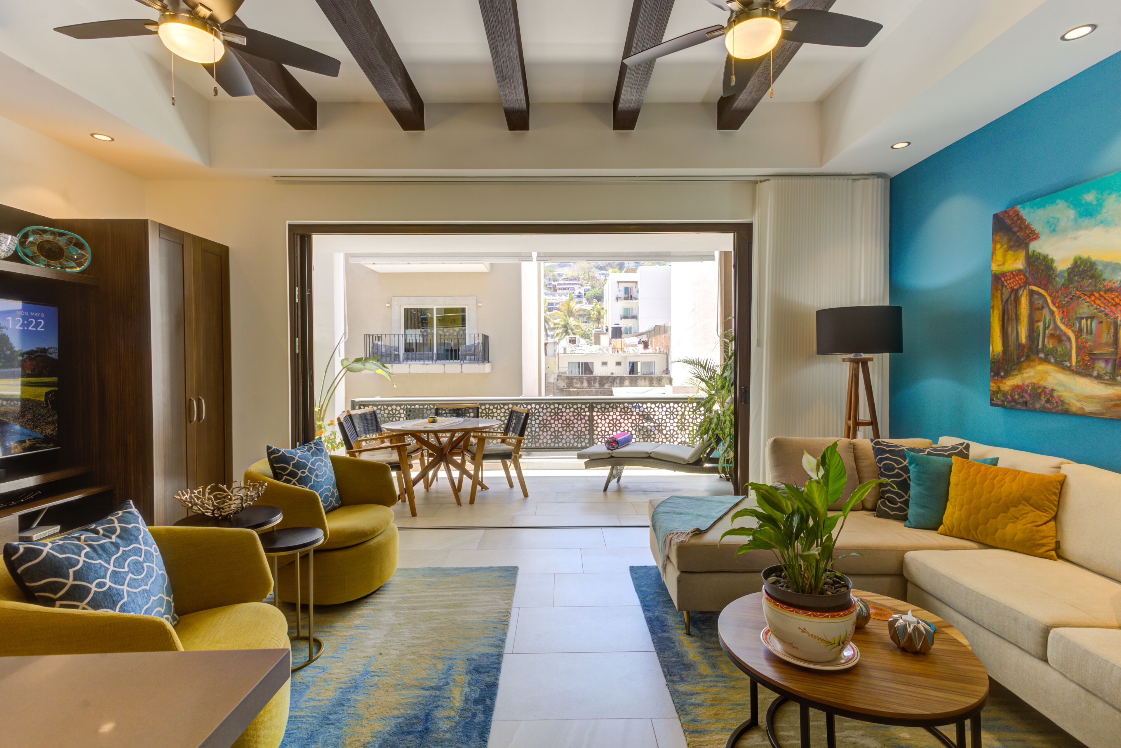 A modern living room with a TV, yellow sofas, a coffee table, and a balcony with a view.