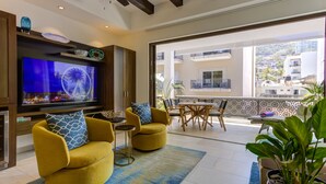 Una sala moderna con televisor de pantalla plana, sillones amarillos, un comedor y un balcón con vistas a edificios y zonas verdes.
