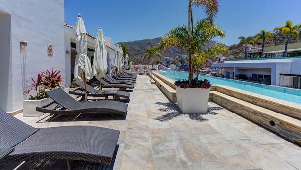 Un área junto a la piscina con sillones de descanso y sombrillas, una piscina y vistas del paisaje circundante.