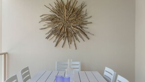 A dining area with a white table and chairs, a decorative wall piece above the table, and a bottle on the table.