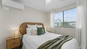 A bedroom with a bed, bedside table, and a window with blinds.