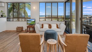 Un salon avec un canapé, deux fauteuils, un téléviseur et une vue sur la plage.