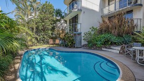 Une piscine entourée d’une végétation luxuriante et un immeuble à plusieurs étages doté de balcons.