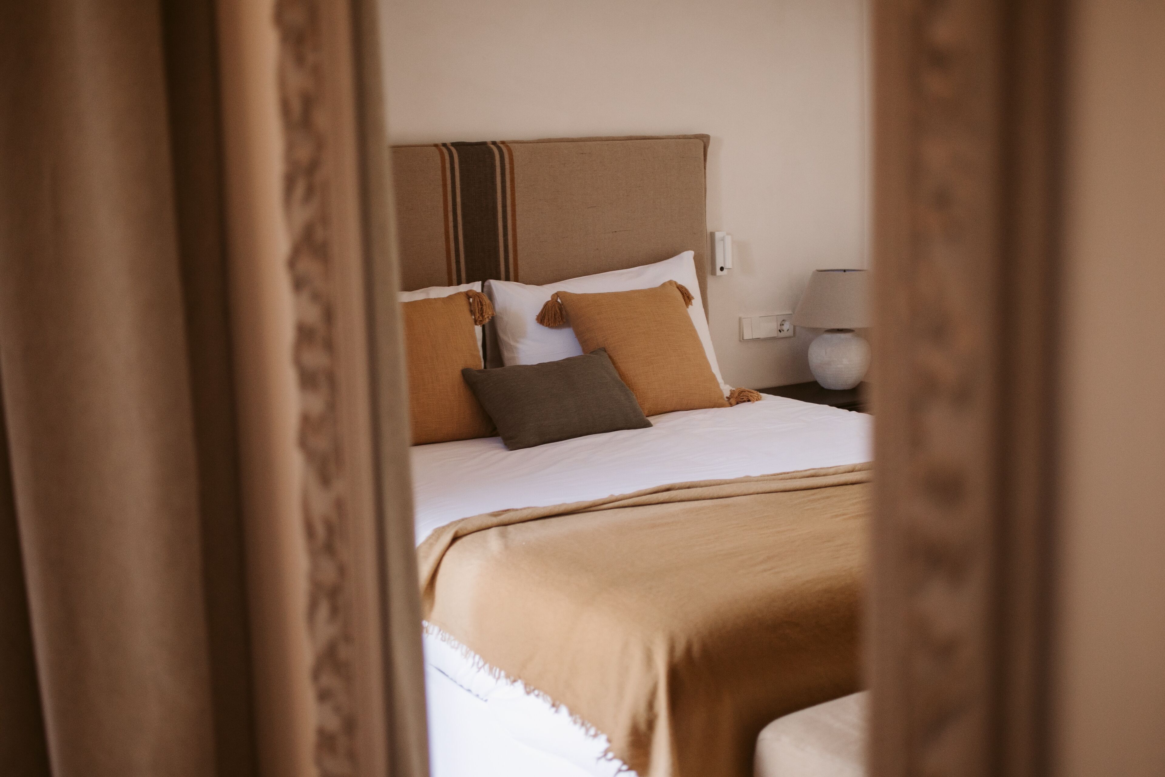 Habitación de hotel con cama, almohadas, cabecero, lámpara y toma de corriente.