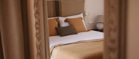 Habitación de hotel con cama, almohadas, cabecero, lámpara y toma de corriente.