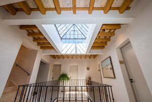 Un interior espacioso con tragaluces, vigas de madera, una escalera y una planta en maceta.